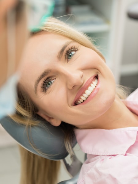 Blonde patient in the dentist chair looking at the dentist and smiling while he explains options